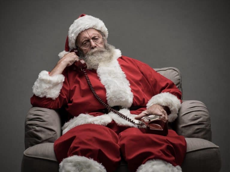 Santa Claus sitting on the armchair and having a phone call, he is holding a receiver and listening